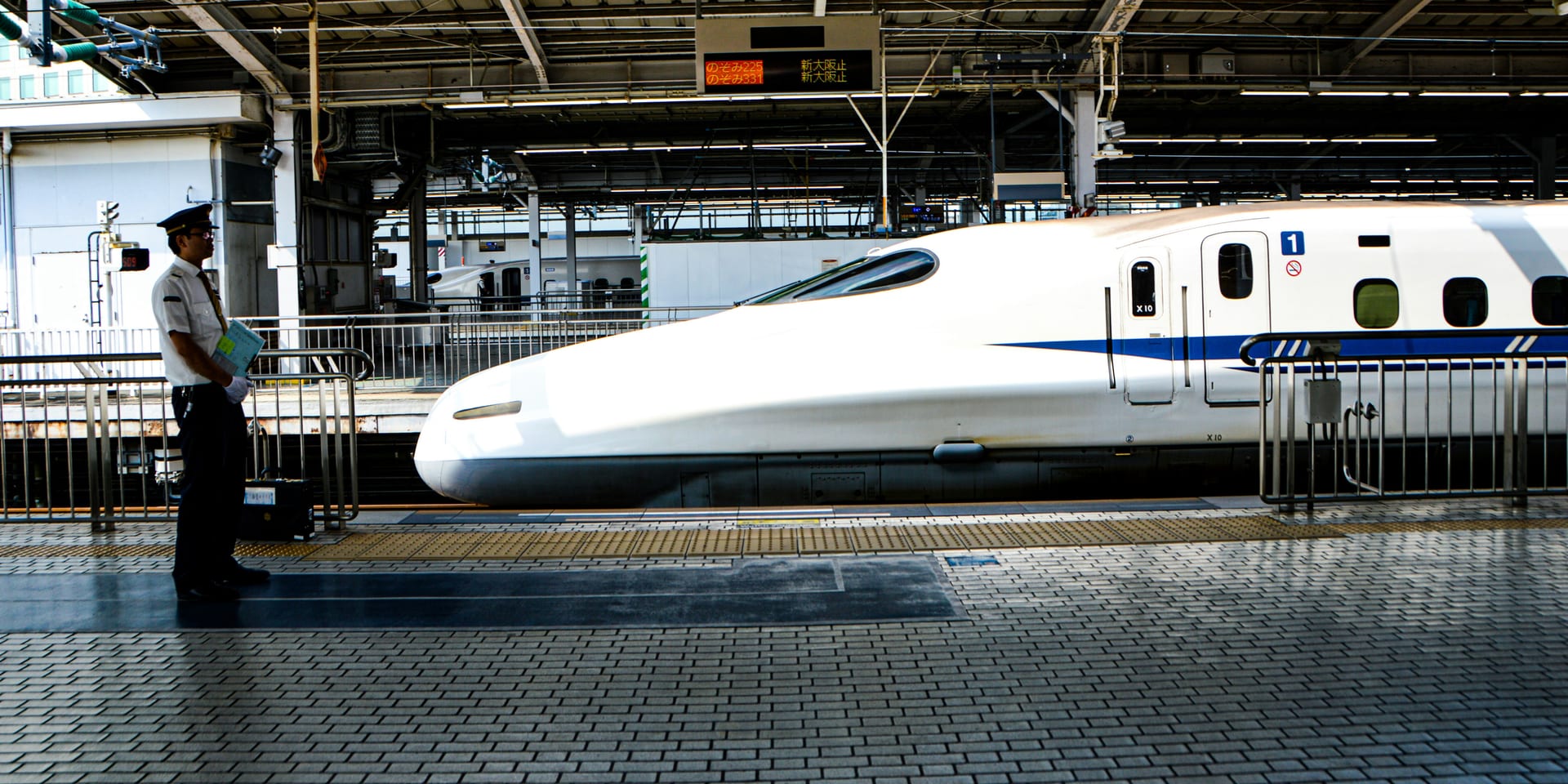 Shinkansen bullet train stopped at a station platform with a conductor standing nearby
